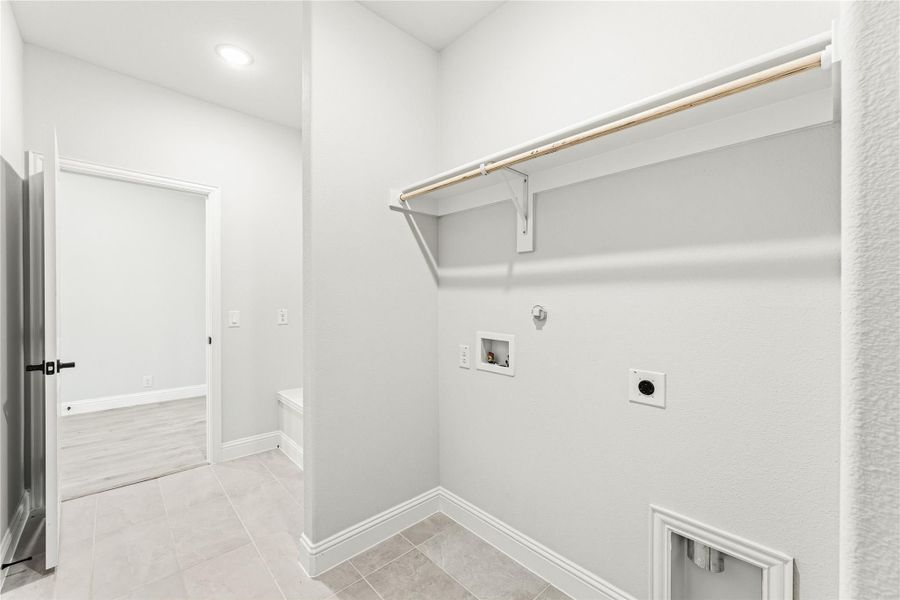 Laundry room with wall-mounted shelf, washer and dryer hookups, and tile flooring