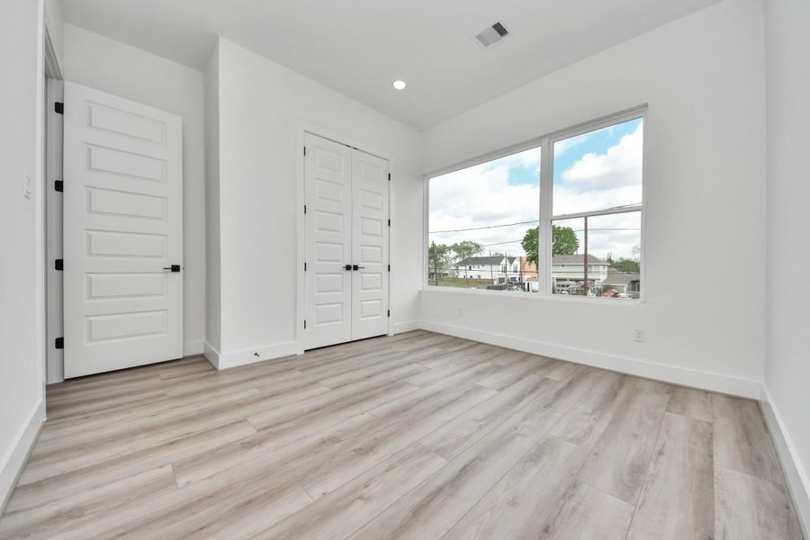 This bright room features large windows, allowing natural light to fill the space. It has light wood flooring and white walls, creating a modern and airy atmosphere. Dual doors add a touch of elegance, and the room offers a neutral palette for customization.