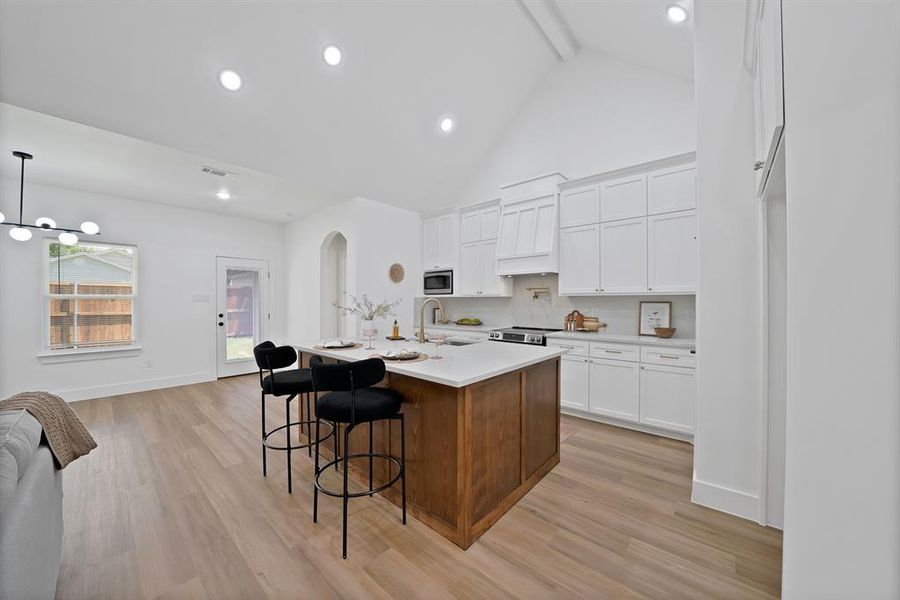 Vaulted ceiling kitchen featuring a central island with countertop seating, wood-finish flooring, white cabinetry, and recessed lighting Vaulted ceiling kitchen featuring a central island with countertop seating, wood-finish flooring, white cabinetry, and recessed lighting