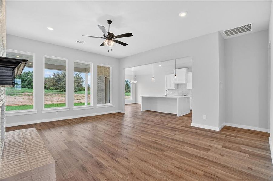 Spacious living area featuring wood-finish flooring, a white brick fireplace with a dark mantel, and a multi-pane window array