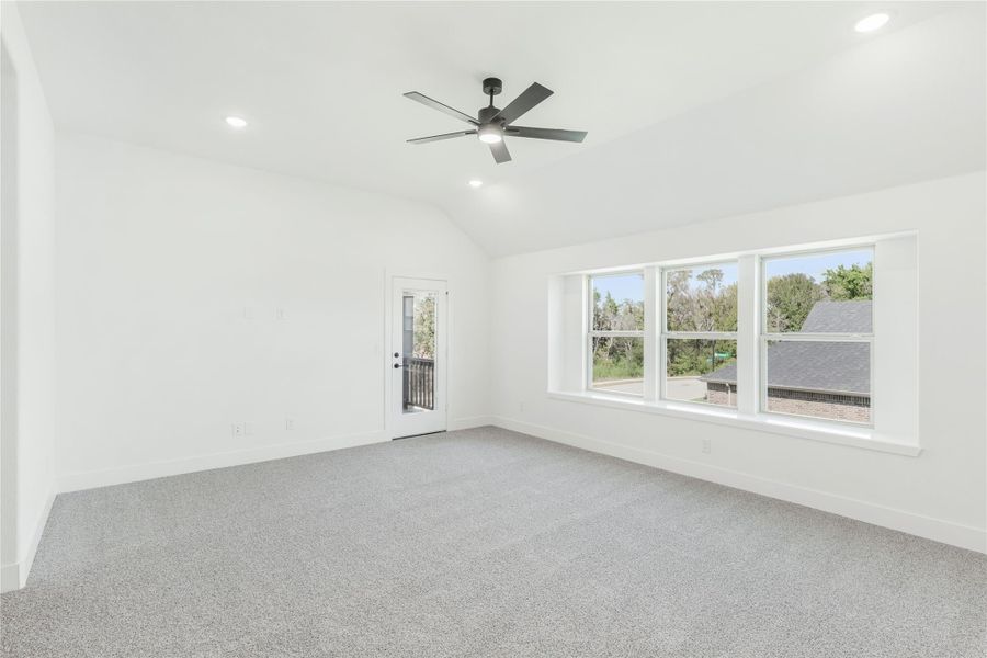 Empty room with vaulted ceiling, ceiling fan, gray carpet, large windows, and a door to an outdoor balcony Empty room with vaulted ceiling, ceiling fan, gray carpet, large windows, and a door to an outdoor balcony