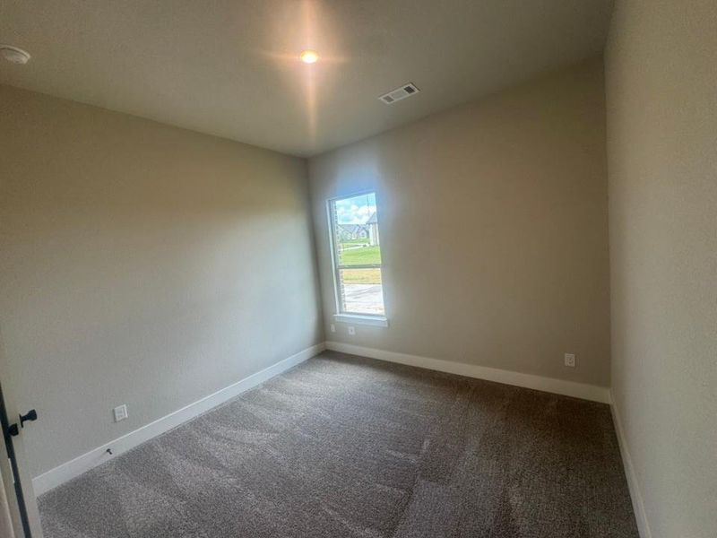Interior room featuring neutral wall tones, textured carpeting, a single window, white baseboards, and a ceiling-mounted light fixture
