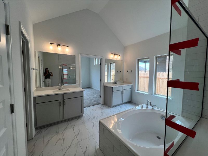 Full bathroom with marble look tiles, a garden tub, two vanities, and high vaulted ceiling Full bathroom with marble look tiles, a garden tub, two vanities, and high vaulted ceiling