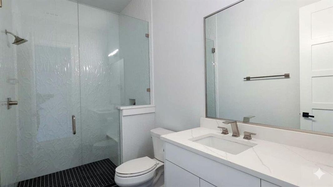 Bathroom featuring a glass-enclosed shower with textured wall tile and dark mosaic floor tile
