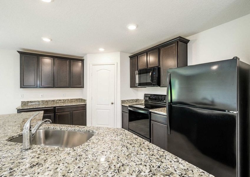 Caladesi plan's kitchen with granite countertops, brown cabinets, black appliances, a pantry & an island that has a sink.