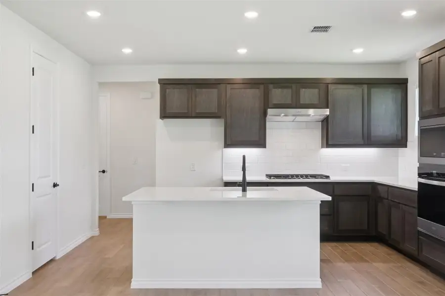 Kitchen with light wood-style flooring, decorative backsplash, light countertops, and recessed lighting