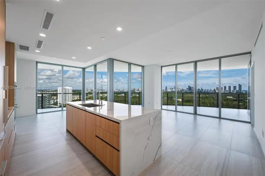 Kitchen featuring a center island with a stone-finish waterfall countertop, integrated cabinetry with wood-finish paneling, recessed lighting, and floor-to-ceiling glass panel walls