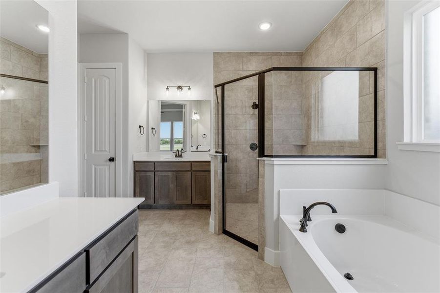 Bathroom featuring a large soaking tub with dark bronze fixtures, a separate glass-enclosed shower with tiled walls, and a double vanity with dark wood-finish cabinetry and light-toned countertops