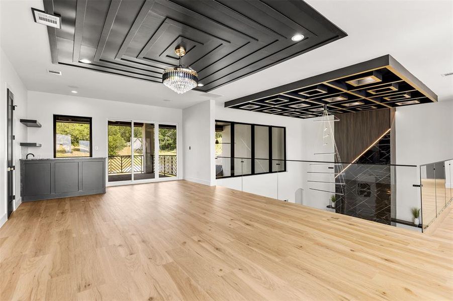 Spacious room featuring light wood-finish flooring, a coffered ceiling with a crystal chandelier, and a built-in wet bar with dark cabinetry