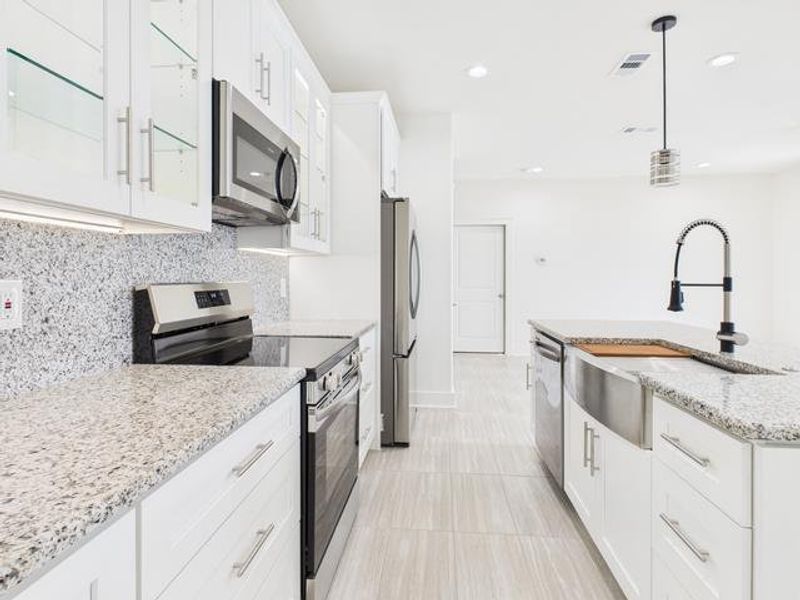 Kitchen featuring stainless steel appliances, white cabinetry, light stone countertops, decorative light fixtures, and an island with sink Kitchen featuring stainless steel appliances, white cabinetry, light stone countertops, decorative light fixtures, and an island with sink
