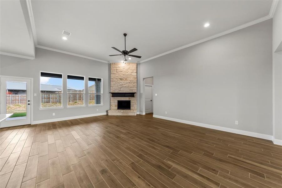 Unfurnished living room with a stone fireplace, crown molding, and ceiling fan