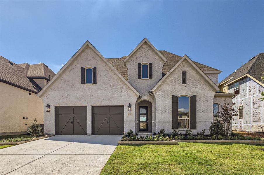 French country home featuring a garage and a front lawn