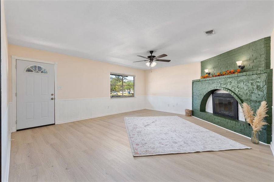 Living area with a wainscoted wall, light wood-type flooring, a fireplace, and ceiling fan