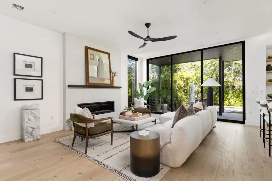 Living area featuring expansive windows, a glass covered fireplace, light wood-style floors, and ceiling fan Living area featuring expansive windows, a glass covered fireplace, light wood-style floors, and ceiling fan