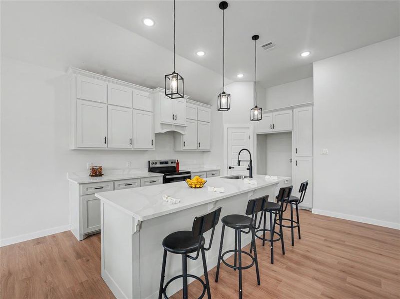 Kitchen with a breakfast bar area, white cabinetry, stainless steel electric range oven, a center island with sink, and light wood-style flooring