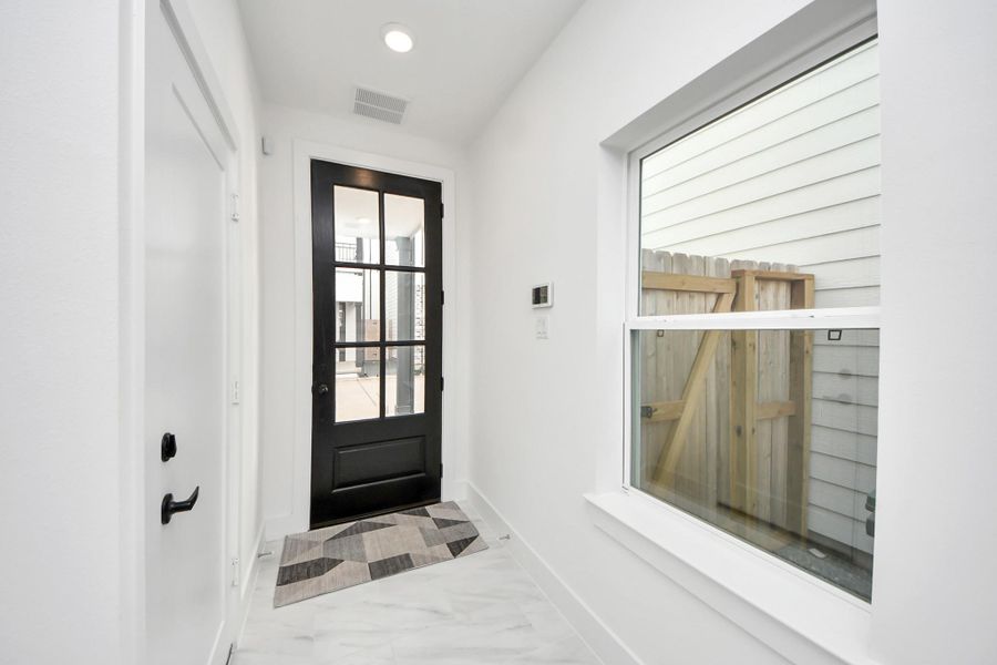 Bright entryway with sleek black-framed glass door and large window, offering natural light and a modern touch.