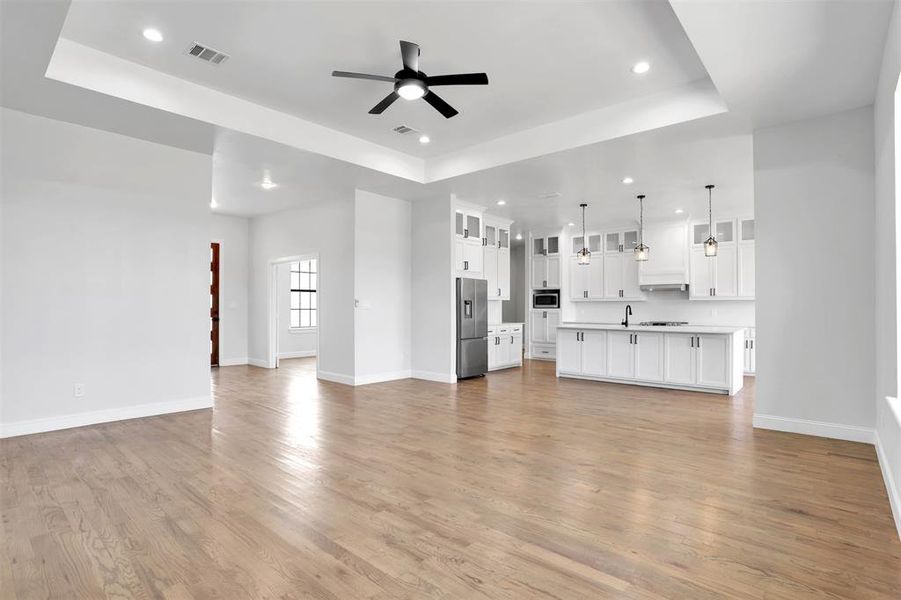 Unfurnished living room with ceiling fan, light hardwood / wood-style flooring, sink, and a tray ceiling