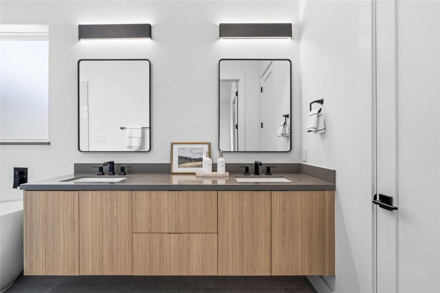 A calm study in symmetry: the primary bath centers a floating, wood-grain vanity with dual under-mount sinks and charcoal quartz surfaces, finished in refined matte-black hardware. Linear sconces and slender framed mirrors provide gallery-level light and proportion, setting a spa-forward tone for unhurried morning rituals. A calm study in symmetry: the primary bath centers a floating, wood-grain vanity with dual under-mount sinks and charcoal quartz surfaces, finished in refined matte-black hardware. Linear sconces and slender framed mirrors provide gallery-level light and proportion, setting a spa-forward tone for unhurried morning rituals.