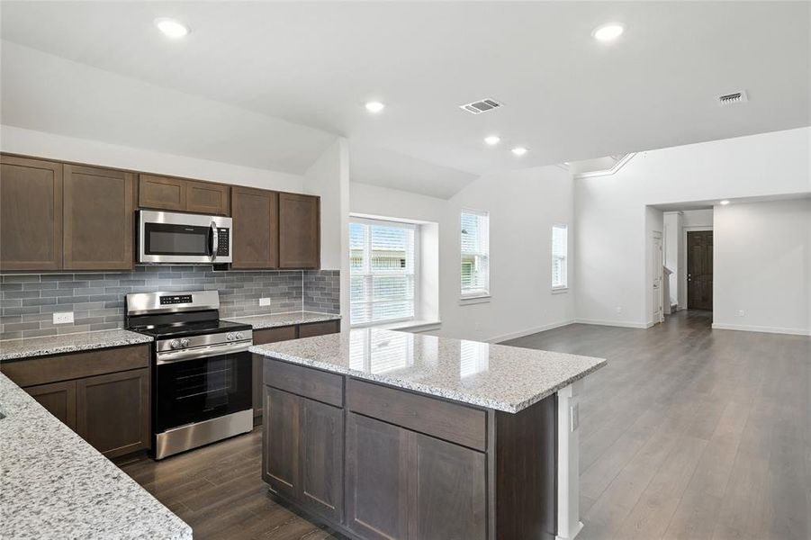 Kitchen featuring stainless steel appliances, vaulted ceiling, backsplash, dark wood-type flooring, and a kitchen island Kitchen featuring stainless steel appliances, vaulted ceiling, backsplash, dark wood-type flooring, and a kitchen island