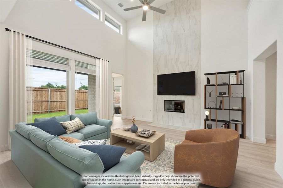 Living room with two-story ceiling, marble fireplace wall, ceiling fan, and large windows overlooking backyard