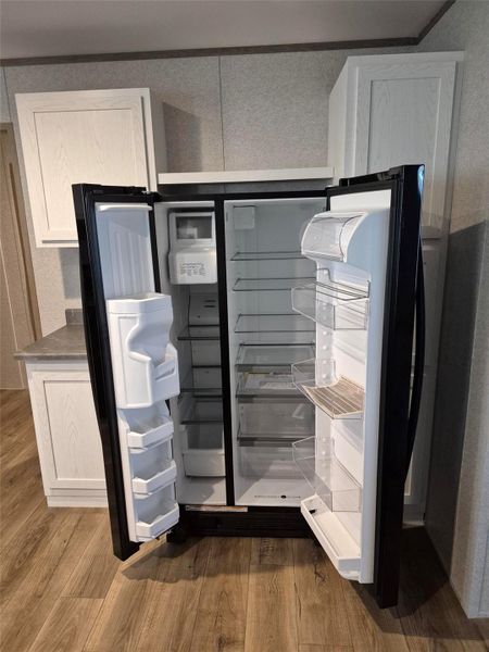 Kitchen view of dark wood-style flooring, white cabinetry, and a textured wall
