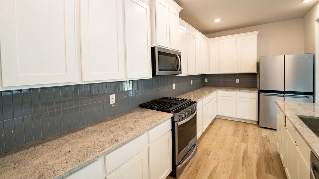Kitchen with stainless steel appliances, light wood-style floors, white cabinetry, backsplash, and recessed lighting Kitchen with stainless steel appliances, light wood-style floors, white cabinetry, backsplash, and recessed lighting