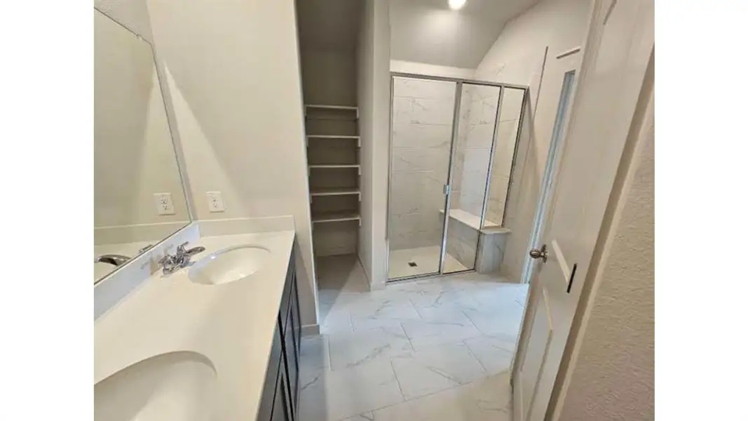 Spacious bathroom featuring a dual vanity with white countertops, a mirrored wall, and a built-in shower with a glass enclosure and bench seating