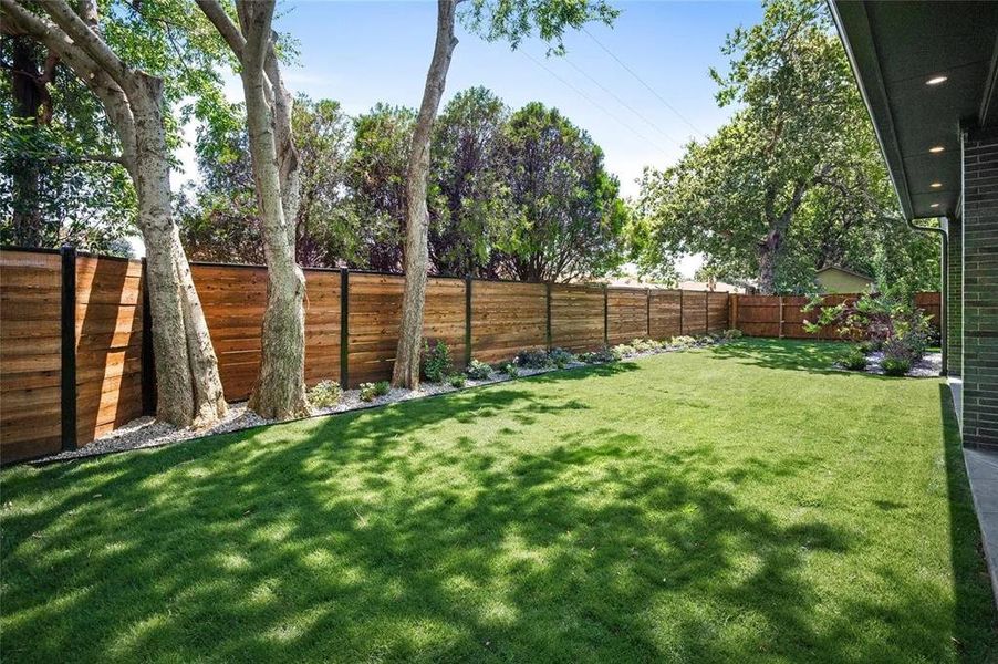 Expansive lawn surrounded by a modern wood-panel fence with dark posts Expansive lawn surrounded by a modern wood-panel fence with dark posts