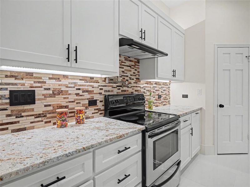 Kitchen with stainless steel range with electric stovetop, white cabinetry, light stone countertops, backsplash, and light tile patterned flooring