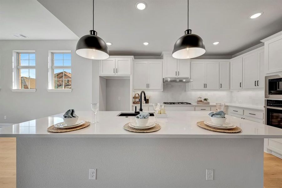 Kitchen featuring white cabinetry, hanging light fixtures, stainless steel appliances, and a large island with sink