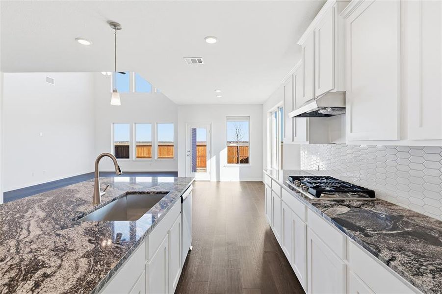 Kitchen featuring white cabinetry, dark patterned countertops, a stainless steel undermount sink with a gooseneck faucet, a built-in gas cooktop, and a geometric tile backsplash