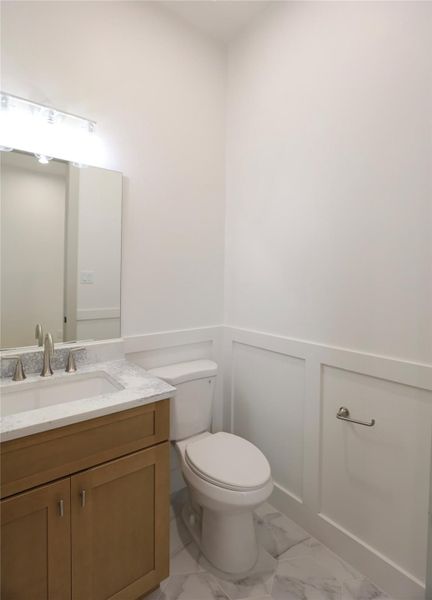 The first-floor powder room exudes charm and dimension, featuring exquisite carpentry with partial wainscoting, elegant hexagon tile flooring, and a designer faucet that adds a refined touch. The first-floor powder room exudes charm and dimension, featuring exquisite carpentry with partial wainscoting, elegant hexagon tile flooring, and a designer faucet that adds a refined touch.