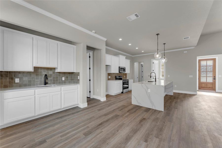 Kitchen featuring decorative backsplash, light stone countertops, an island with sink, stainless steel appliances, and decorative light fixtures