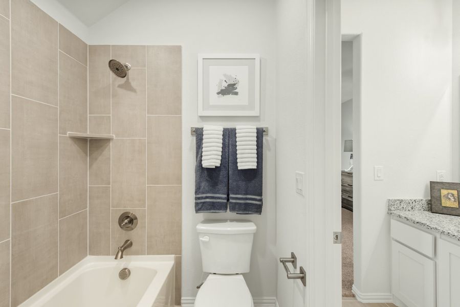 Bathroom with tiled tub and shower, toilet, white vanity with granite countertop, and white walls
