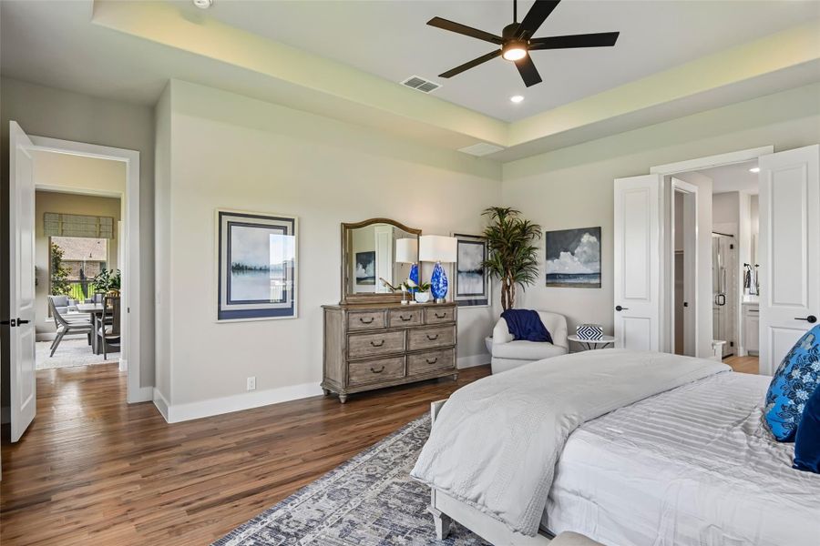 Master bedroom with tray ceiling, ceiling fan, hardwood floors, and wood dresser with mirror Master bedroom with tray ceiling, ceiling fan, hardwood floors, and wood dresser with mirror