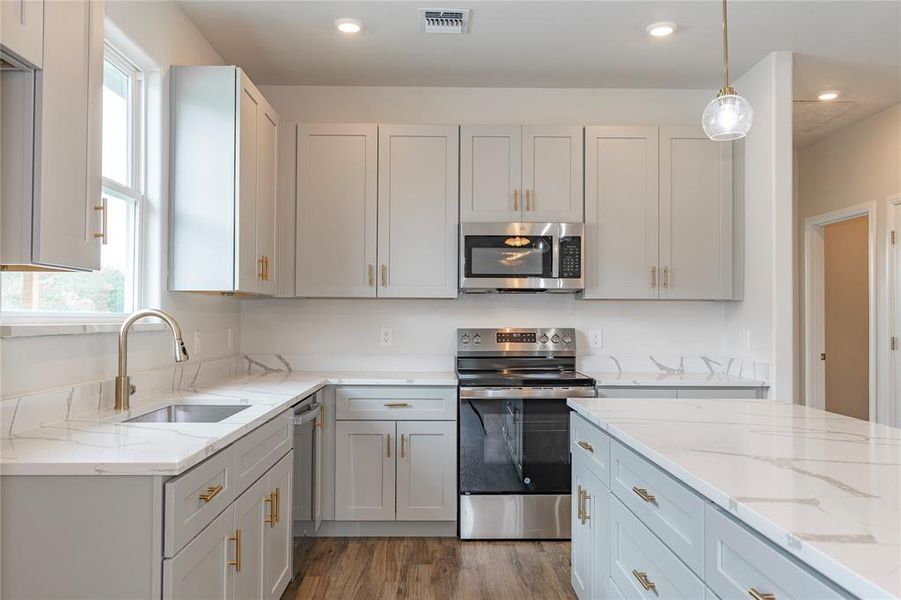 Kitchen with decorative light fixtures, appliances with stainless steel finishes, sink, hardwood / wood-style flooring, and light stone counters