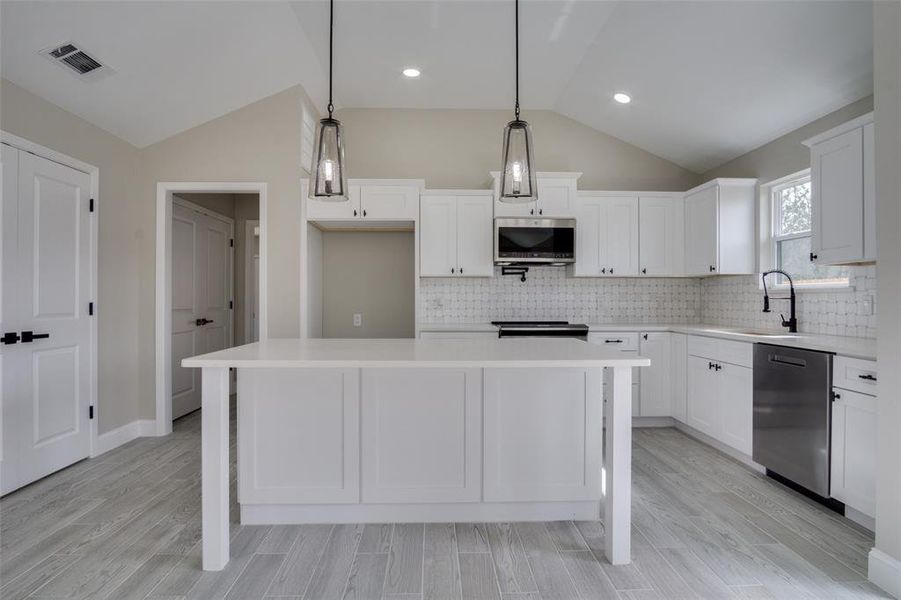 Kitchen with visible vents, a center island, light countertops, lofted ceiling, and appliances with stainless steel finishes