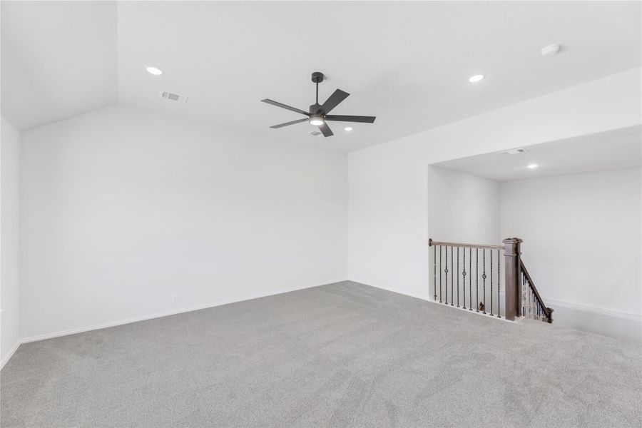Open upstairs living area with gray carpet, ceiling fan, and wood staircase railing Open upstairs living area with gray carpet, ceiling fan, and wood staircase railing