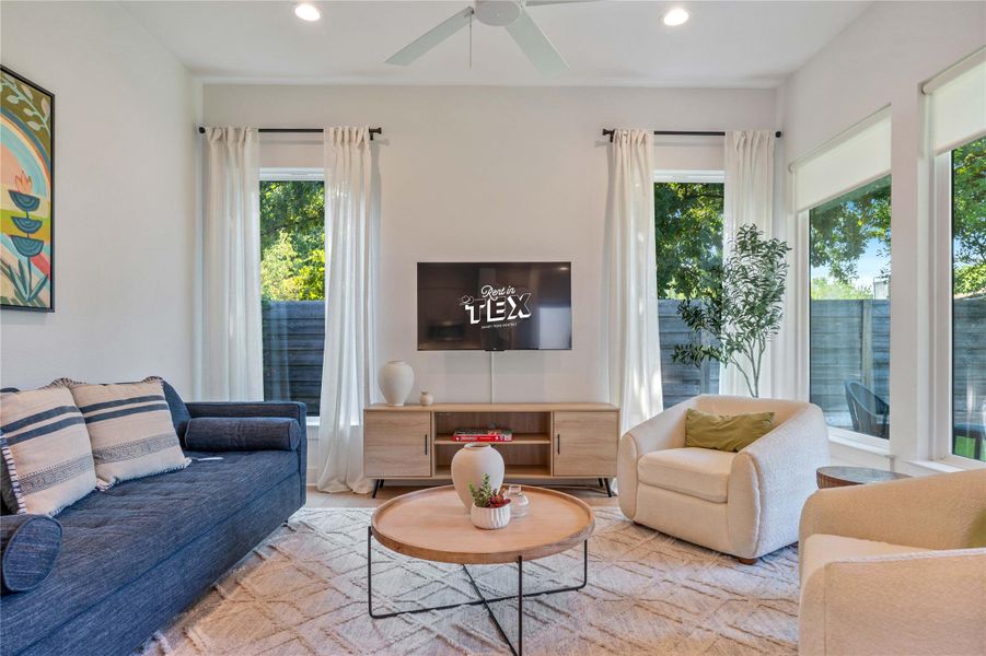 Tall windows frame peaceful backyard views in this inviting living area featuring recessed lighting.