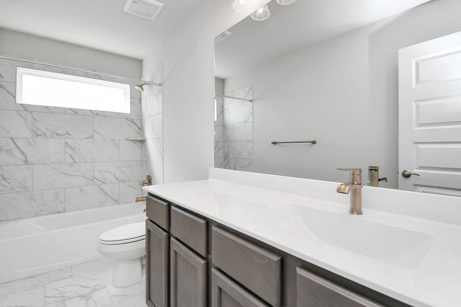 The secondary bath boasts stylish tile flooring, a bath/shower combo with a sleek tile surround, light wood cabinets, and a stunning light countertop. Sample photo of completed home with similar floor plan. Actual colors and selections may vary.