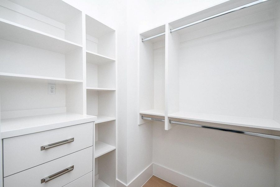 This is a spacious, modern walk-in closet with white shelving, drawers, and hanging rods, offering ample storage and organization options.
