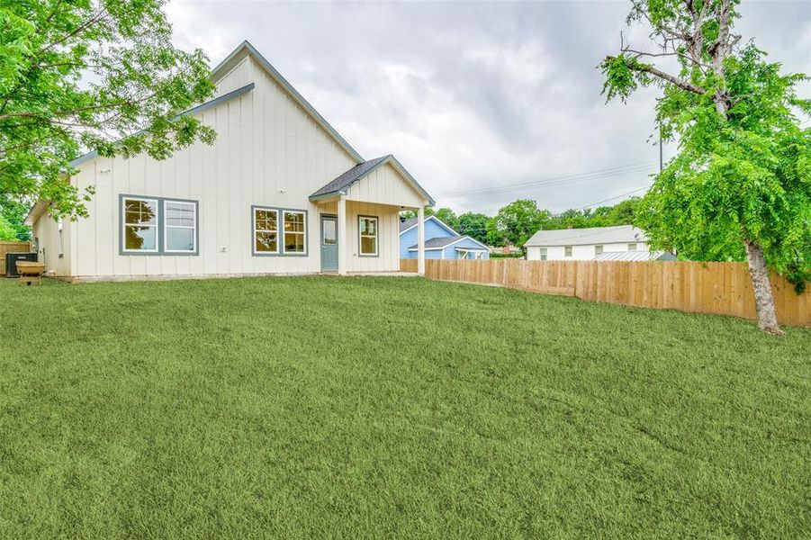 Rear view of house featuring a lawn, board and batten siding, and fence
