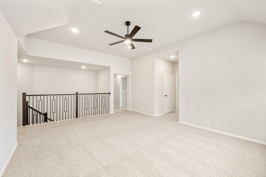 Open upstairs loft with carpet, ceiling fan, and black metal stair railing along open landing