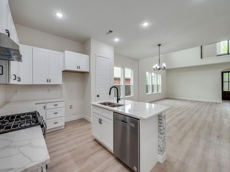 Kitchen with appliances with stainless steel finishes, a sink, a chandelier, light stone countertops, and recessed lighting