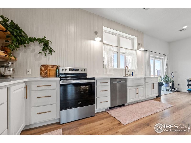 Bright and functional kitchen with stainless steel appliances, timeless white cabinetry, open shelving, and filled with natural light.