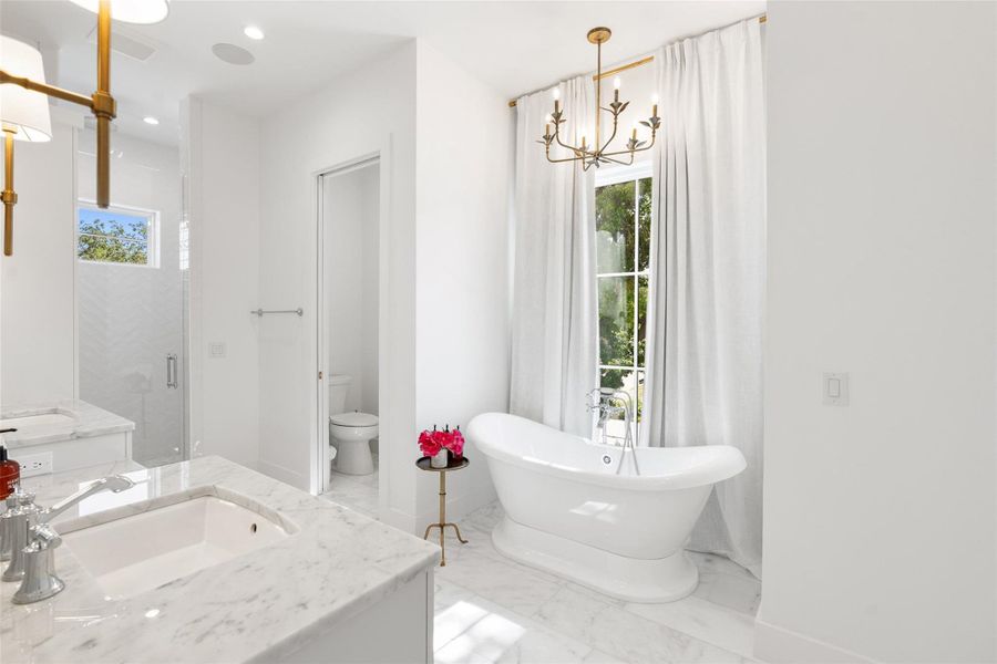 A freestanding soaking tub and dual vanity sinks define this elegant bathroom, featuring marble flooring and abundant natural light. A freestanding soaking tub and dual vanity sinks define this elegant bathroom, featuring marble flooring and abundant natural light.