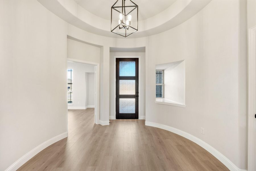 Round foyer with tray ceiling, geometric chandelier, dark glass front door, and light hardwood floors