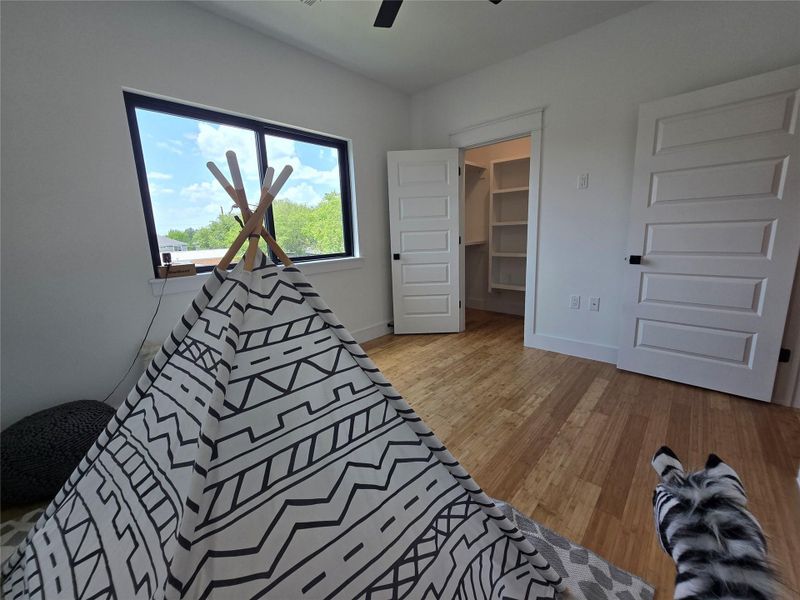 Bedroom with wood finished floors, a spacious closet, and a ceiling fan