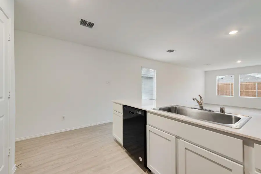 Kitchen featuring dishwasher, light countertops, a sink, and white cabinetry