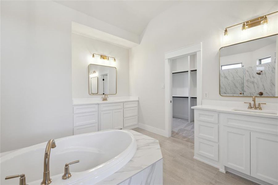 Bathroom featuring lofted ceiling, tiled tub, tile patterned floors, and dual vanity